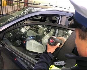 Policjant mierzy przejrzystość przedniej bocznej szyby w samochodzie