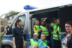 policjantka stoi przy radiowozie, wewnątrz siedzą dzieci