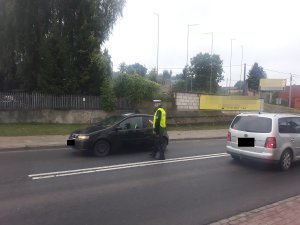 policjant stojąc z alkomatem przy pojeździe bada stan trzeźwości kierowcy