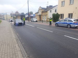 policjant stojąc z alkomatem przy pojeździe bada stan trzeźwości kierowcy