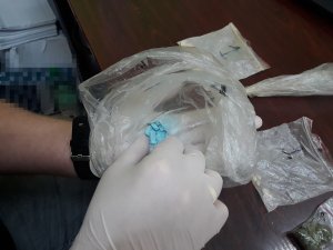 policjant trzyma w ręku woreczek z niebieskimi tabletkami ekstazy
