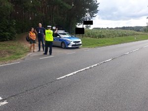 policjant i przedstawiciele służb stoją przy drodze w miejscu wypadku drogowego, na poboczu stoi radiowóz