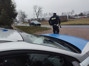 policjant stoi przy drodze i obserwuje jadące pojazdy